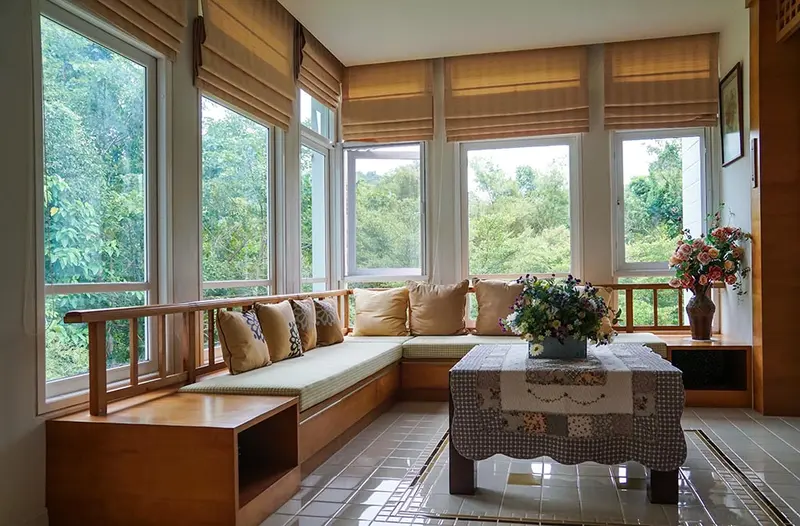 Estores romanos beige en las ventanas de una galería de madera con banco