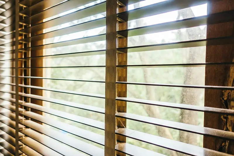 Luz cálida entrando por una persiana veneciana de madera, primer plano
